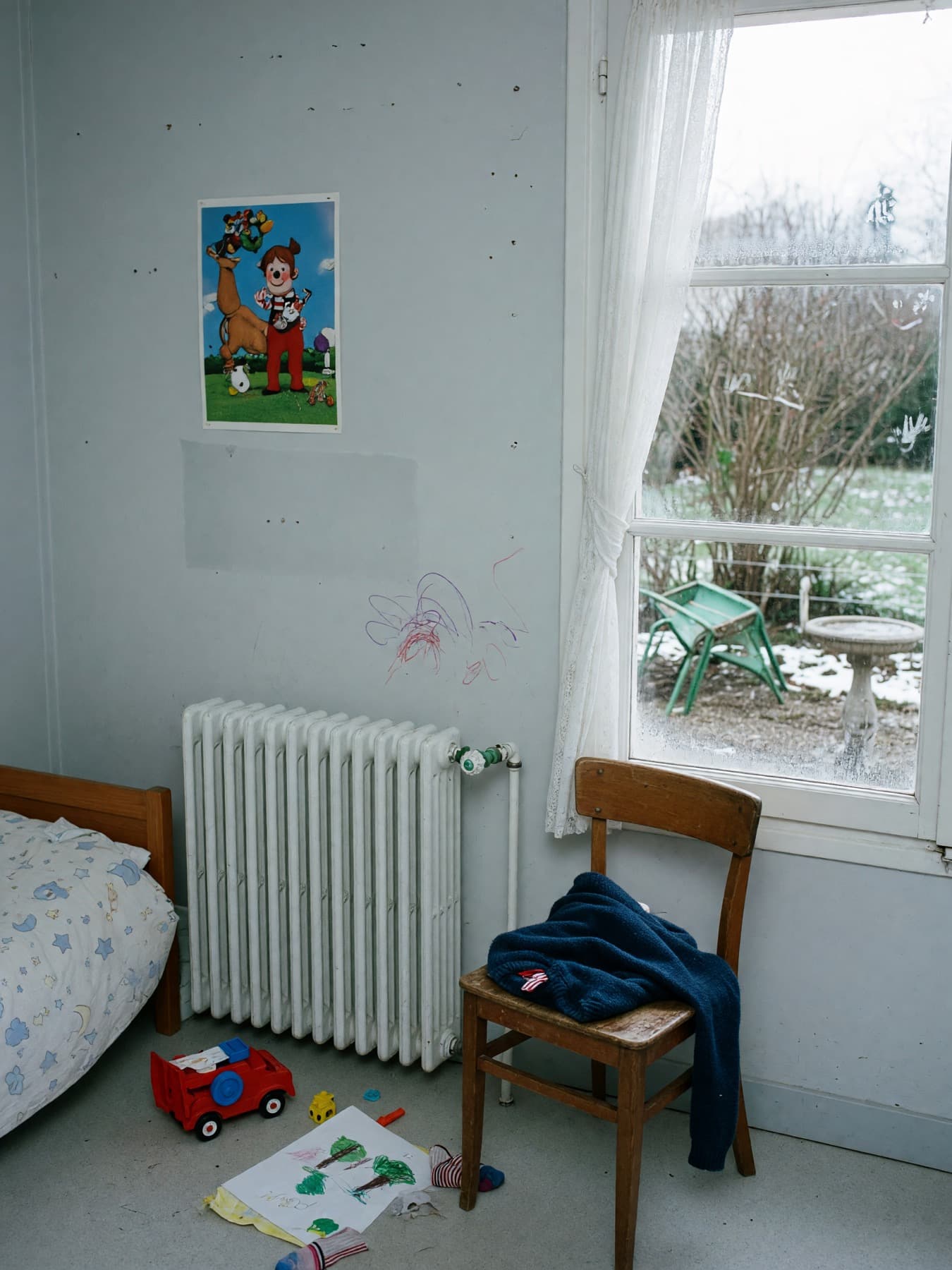 Photographie de démonstration : chambre d’enfant, radiateur en fonte, jardin d’hiver derrière la vitre