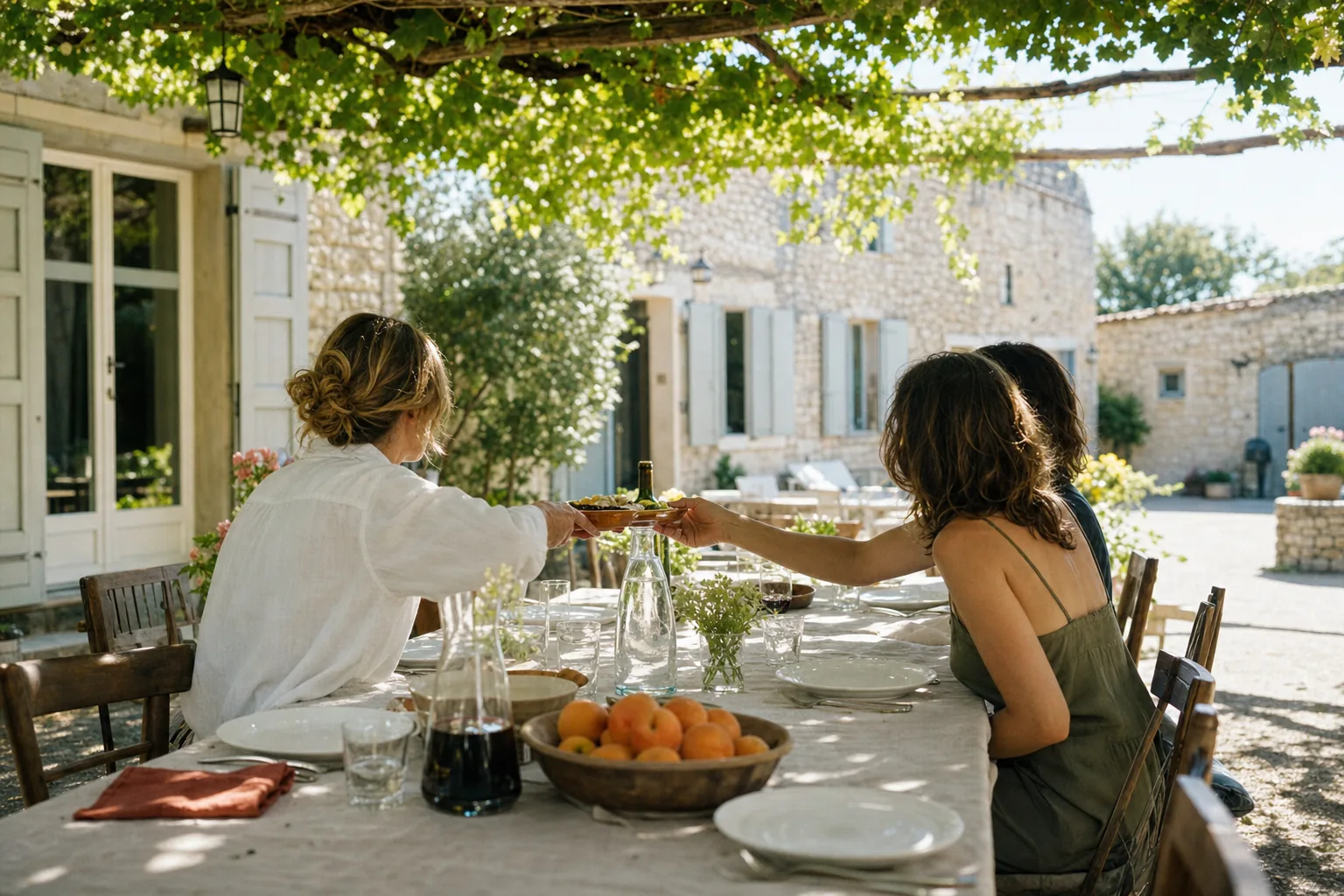 La longue table dressée sous la treille au soleil couchant, carafe de vin à contre-jour et convives vus de dos